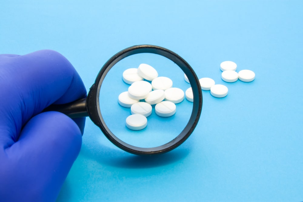 hand in blue glove holding microscope looking at pharmaceutical pills